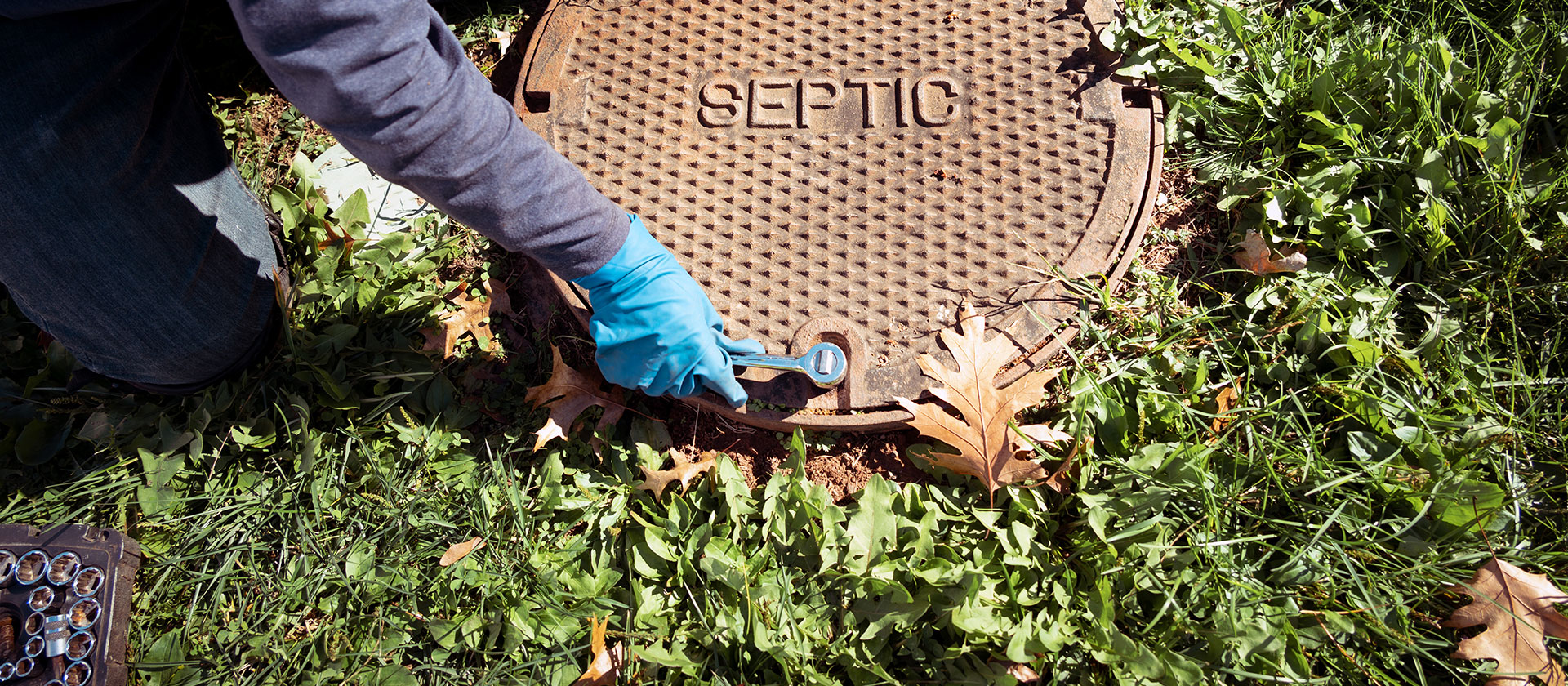 person opening septic hole with wrench